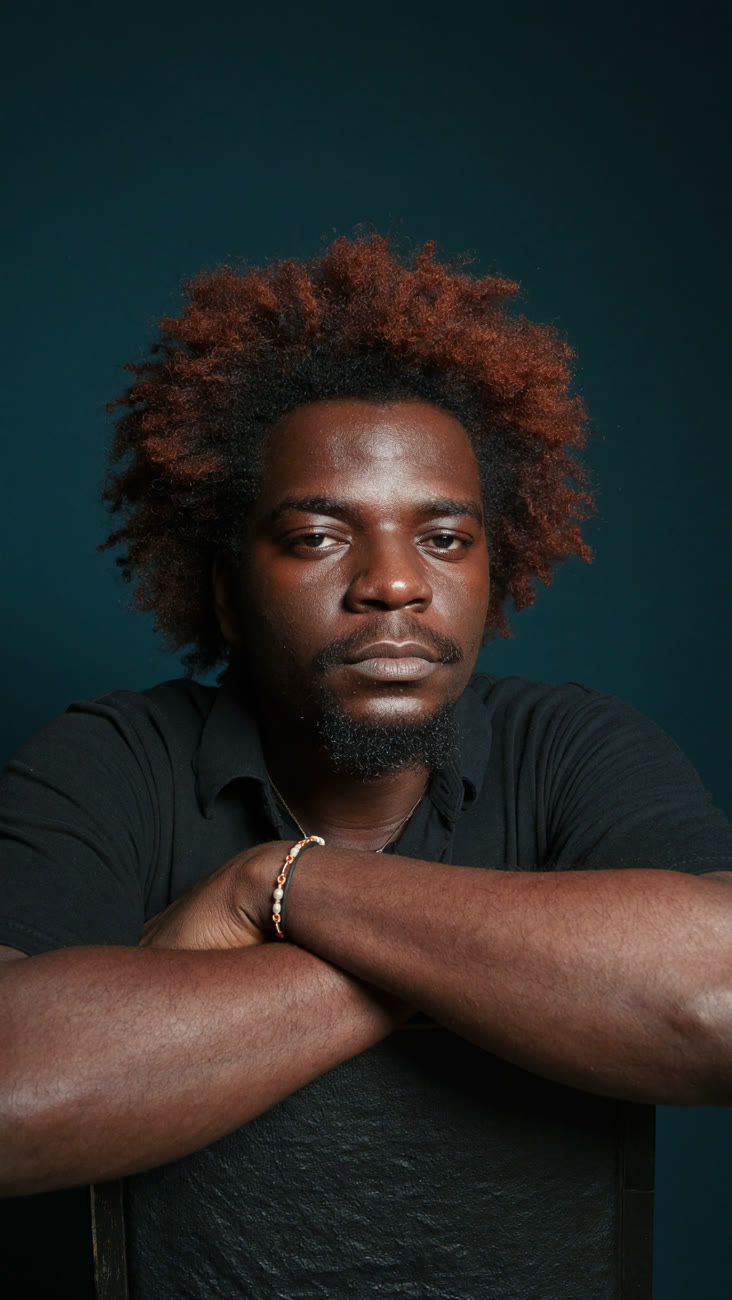 Portrait of Idowu Damilola Charles, founder of Kaniverse, arms folded over a chair back against a deep teal backdrop